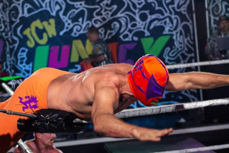 Masked luchador diving through the ropes