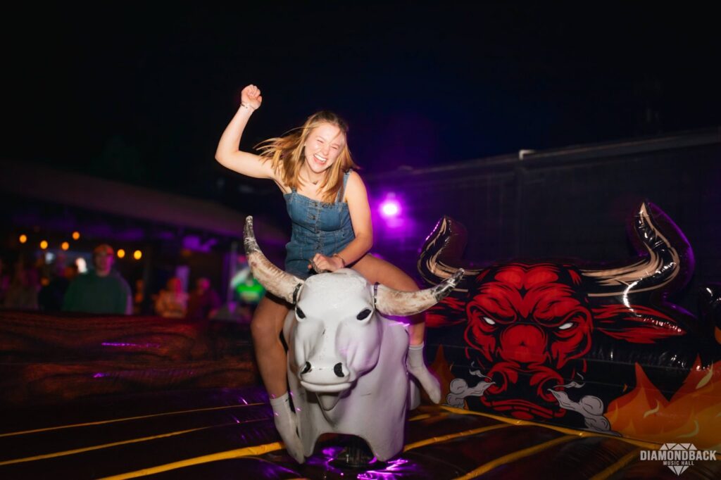 Guest riding a mechanical bull at a themed night at Diamondback Music Hall